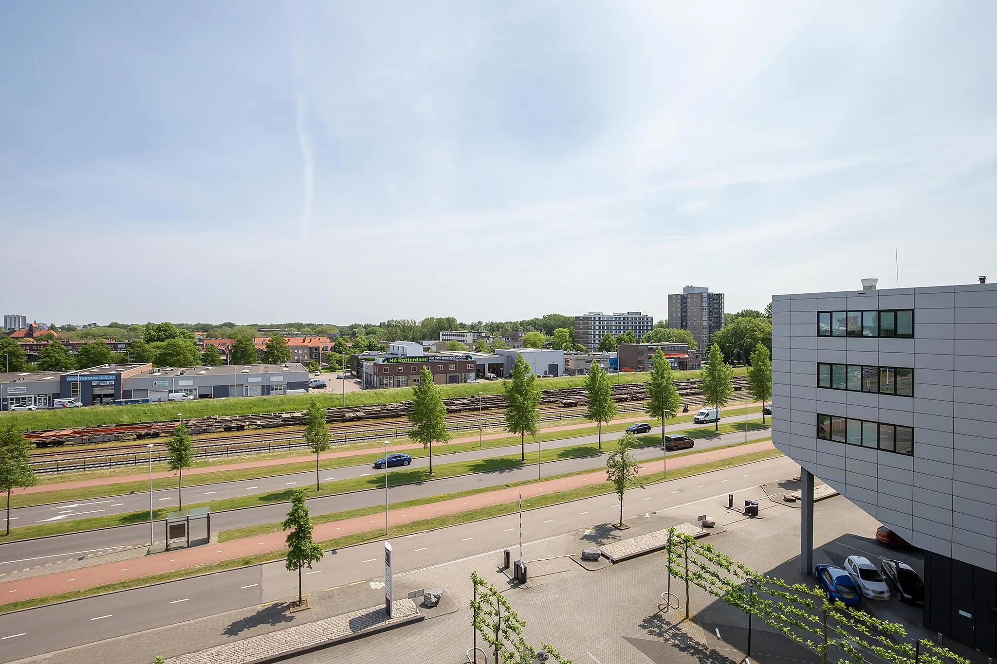 Luchtige straat- en stadsaanblik van Waalhaven-Oostzijde met wegen, spoorlijnen, bedrijfspanden en flats op een zonnige dag.